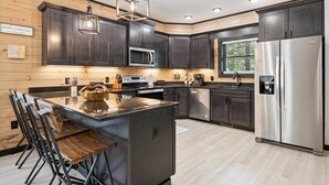 Une cuisine moderne avec des meubles en bois foncé, des appareils électroménagers en acier inoxydable et un îlot central doté de tabourets de bar.