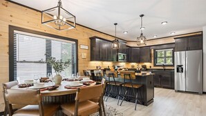 Une cuisine moderne dotée de meubles en bois, d’appareils électroménagers en acier inoxydable et d’un coin repas avec une table ronde et des chaises.