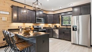 A modern kitchen with dark wood cabinets, stainless steel appliances, and a central island with bar stools. - New Cabin w Indoor Swim Spa Hot Tub Gameroom (Pigeon Forge)