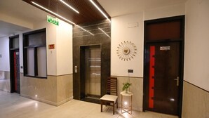 Et hotel lobby med elevator, en stol, et lille bord med en plante og et vægur.
