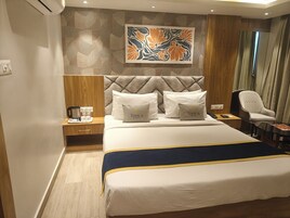 A hotel room with a large bed, a headboard with a geometric pattern, a coffee maker on the nightstand, and a chair near the window.