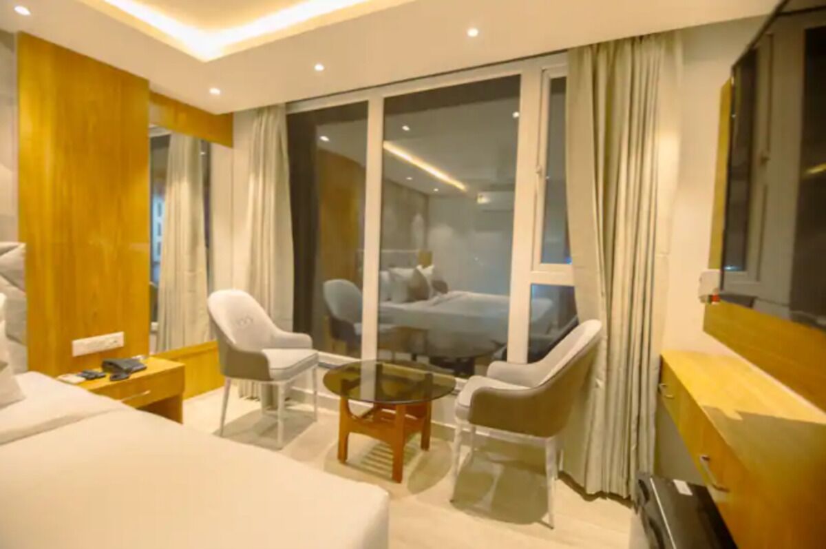 A hotel room with a bed, a glass table, two chairs, a nightstand, and a large window with curtains.