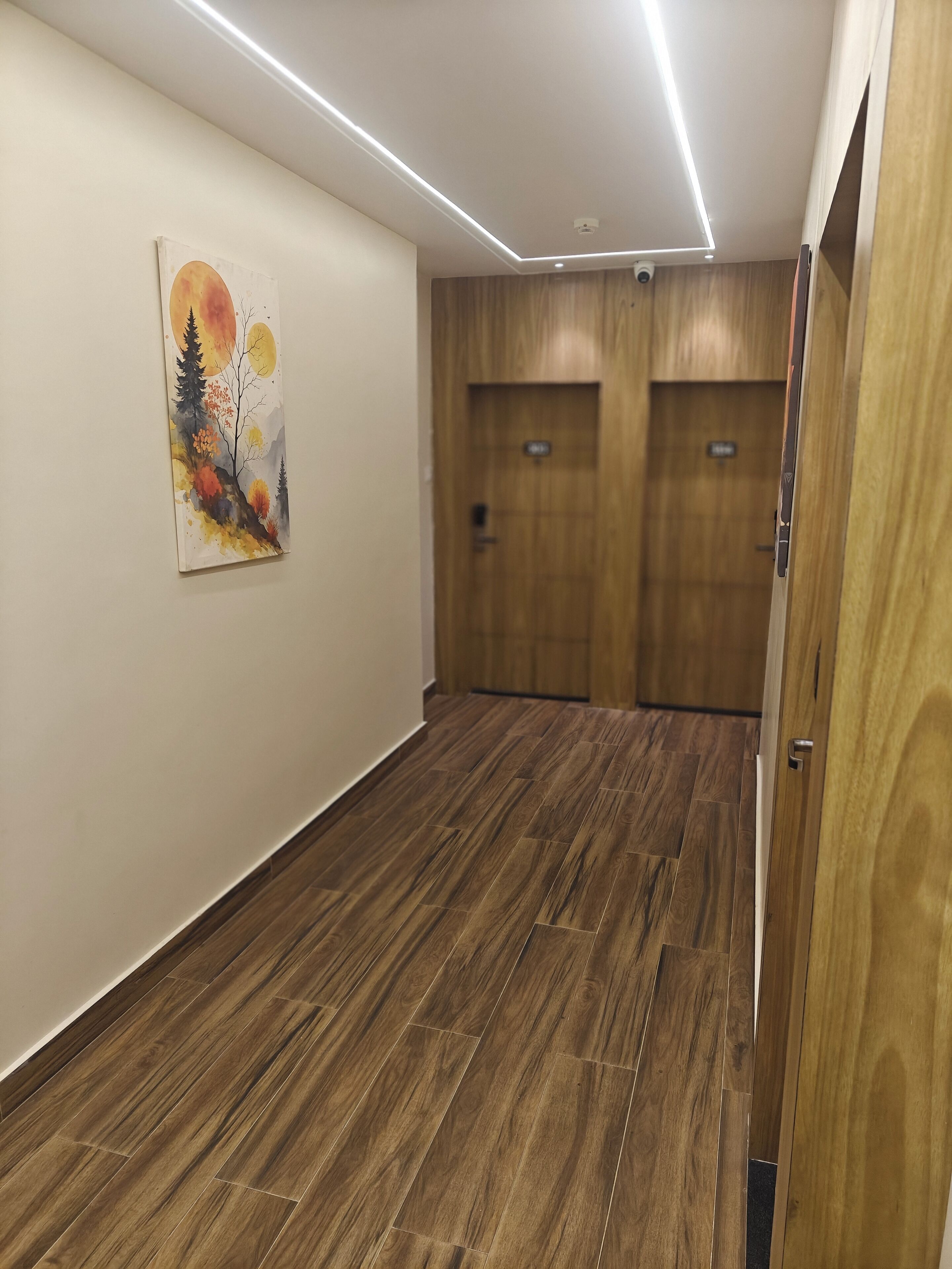Un pasillo con suelo de madera, un cuadro en la pared y dos puertas de madera.