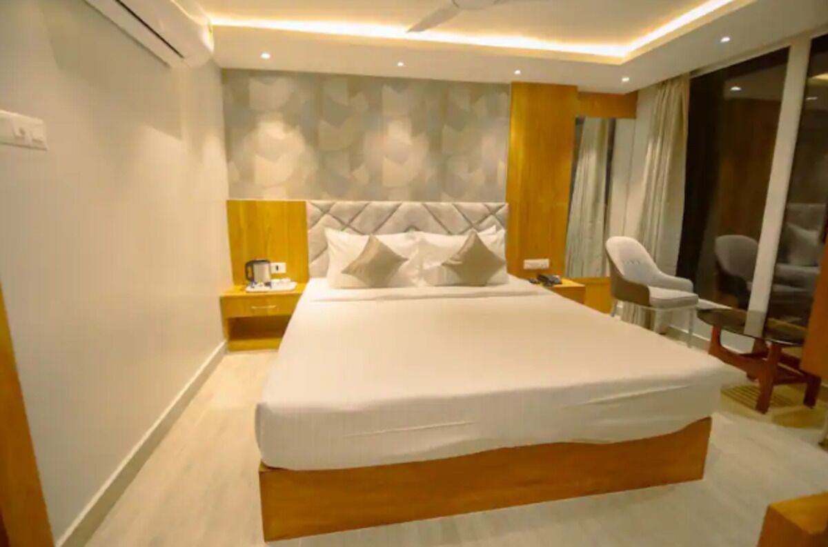 Quarto de hotel moderno com uma cama grande, uma mesinha de cabeceira, uma cadeira e vista para o exterior.