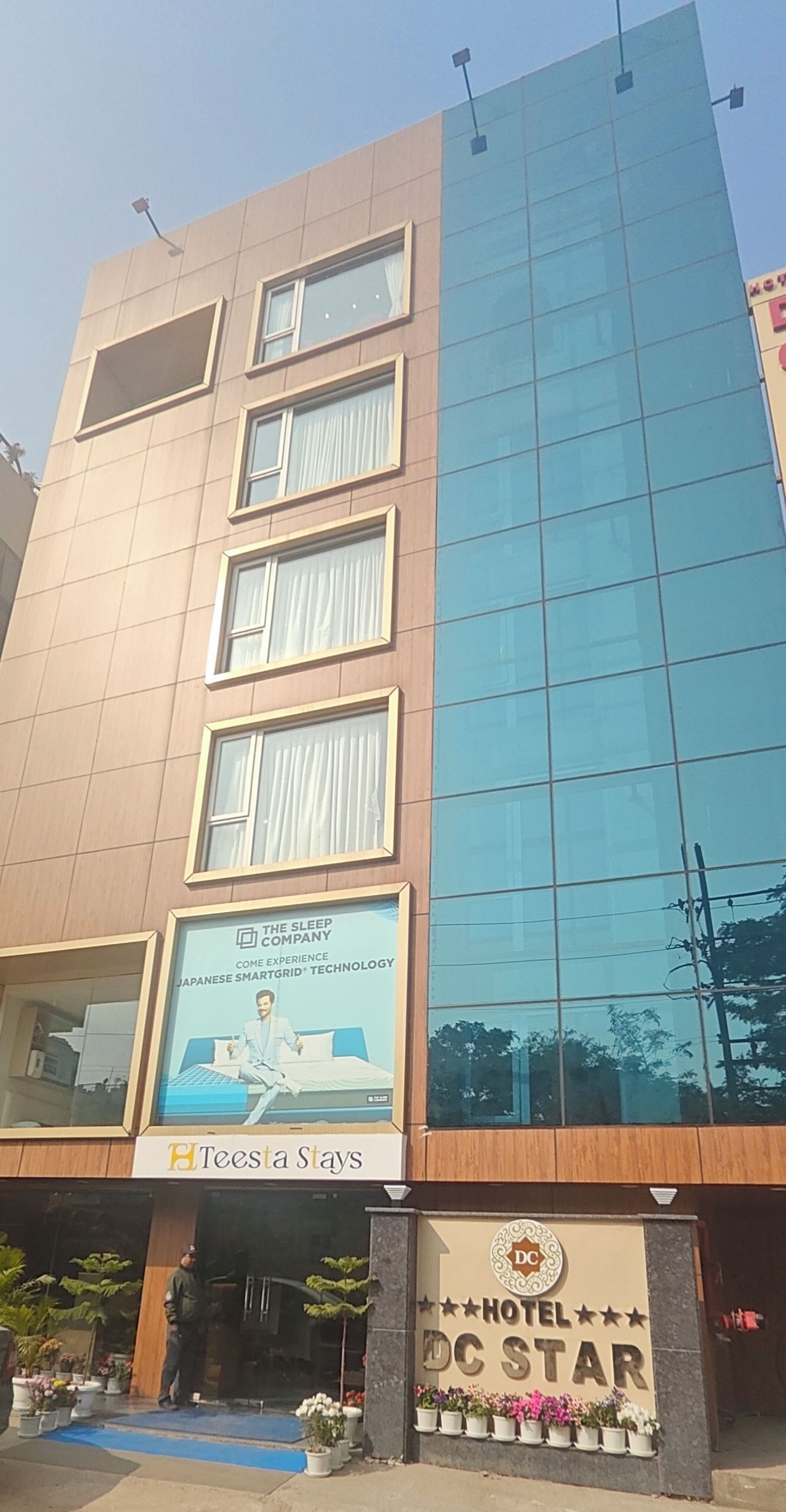 A hotel with a modern facade, featuring a large glass window on the right side and a sign for 'Teesta Stays' on the left.