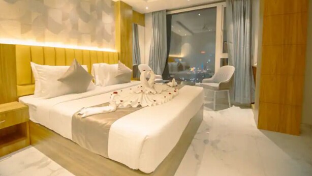 A modern hotel room with a large bed, a seating area, and a view of the cityscape. - Hotel Teesta Stays Kolkata (Barasat)