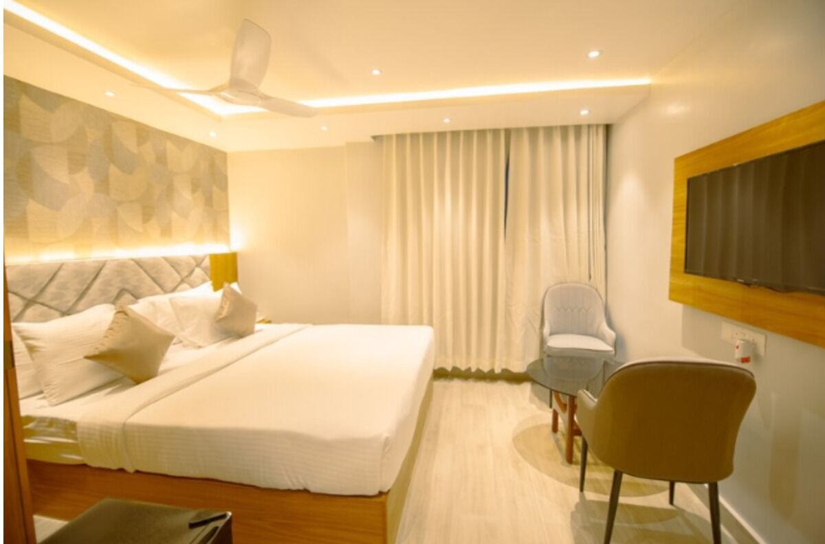 A hotel room with a bed, a chair, a desk, a window with curtains, and a ceiling fan.