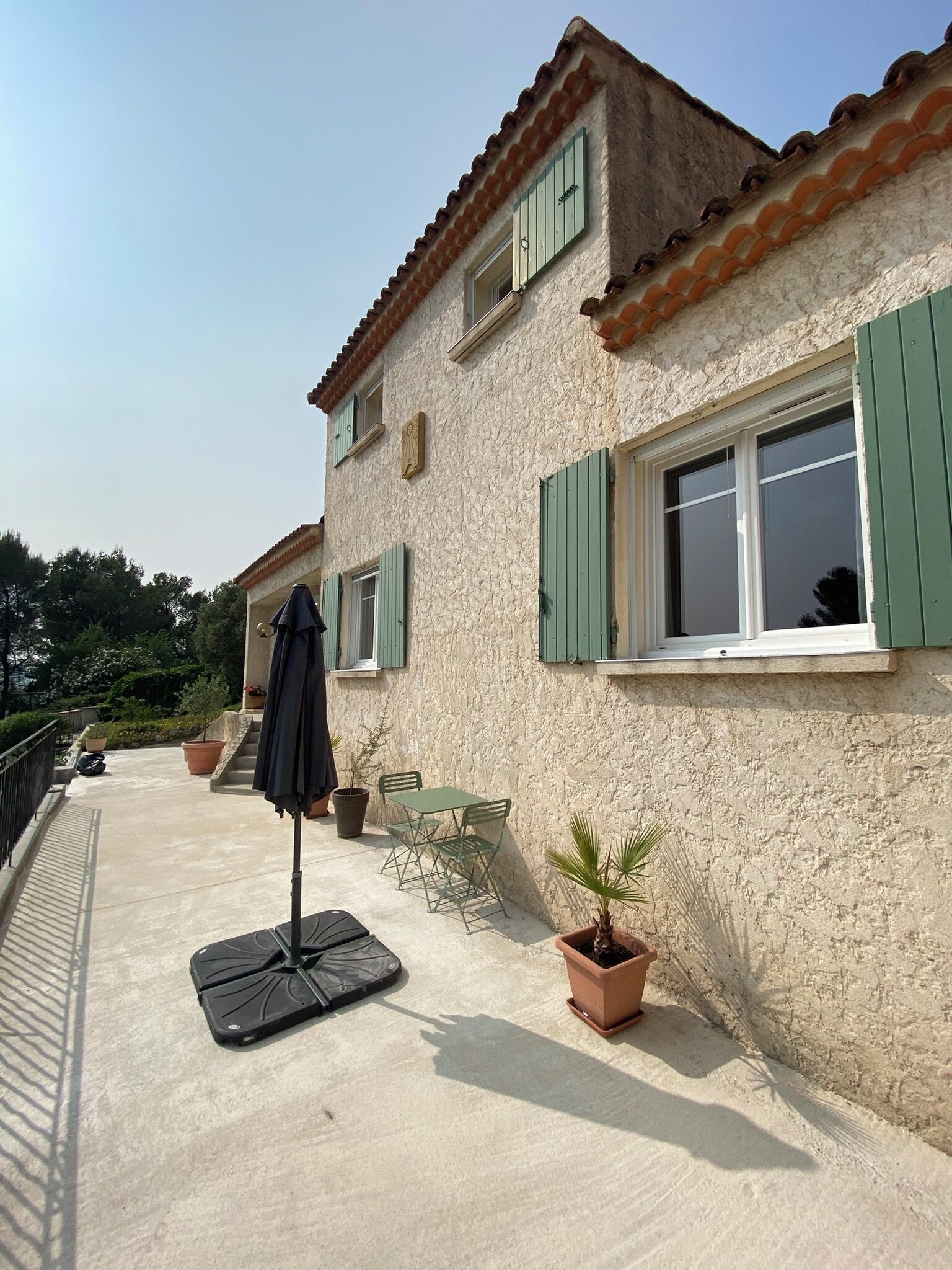 A building with a textured facade, green shutters, and a small balcony with a table and chairs.
