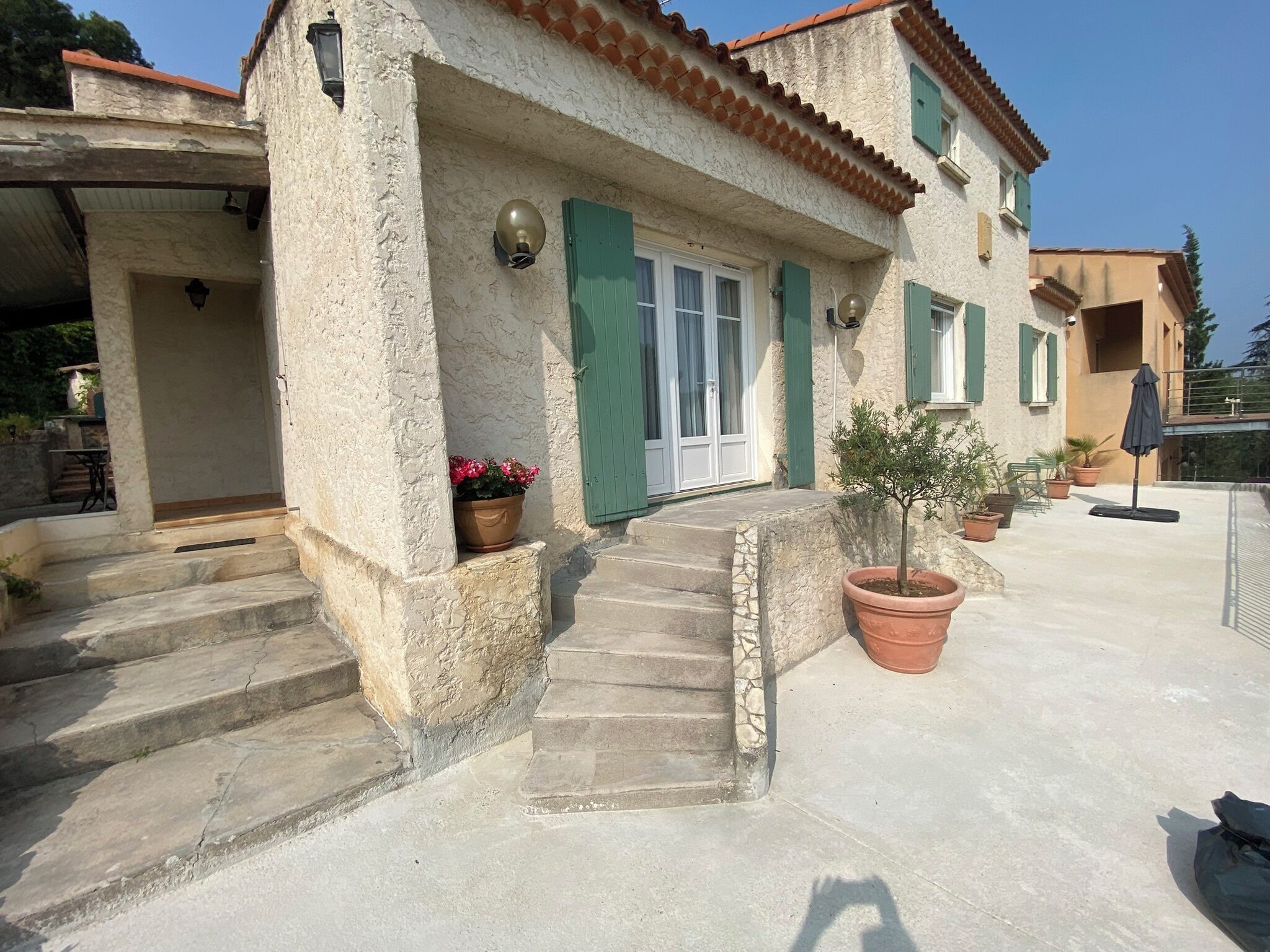 A rustic building with a stone facade, green shutters, and a small staircase leading to the entrance.