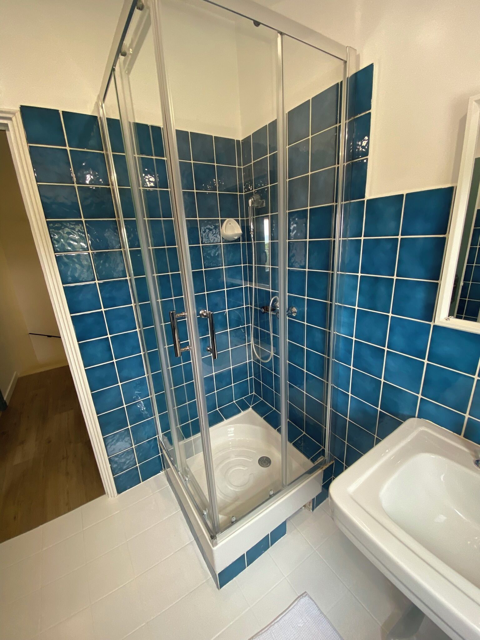 Une salle de bain avec une douche à parois de verre, une baignoire blanche et des murs recouverts de carreaux bleus.