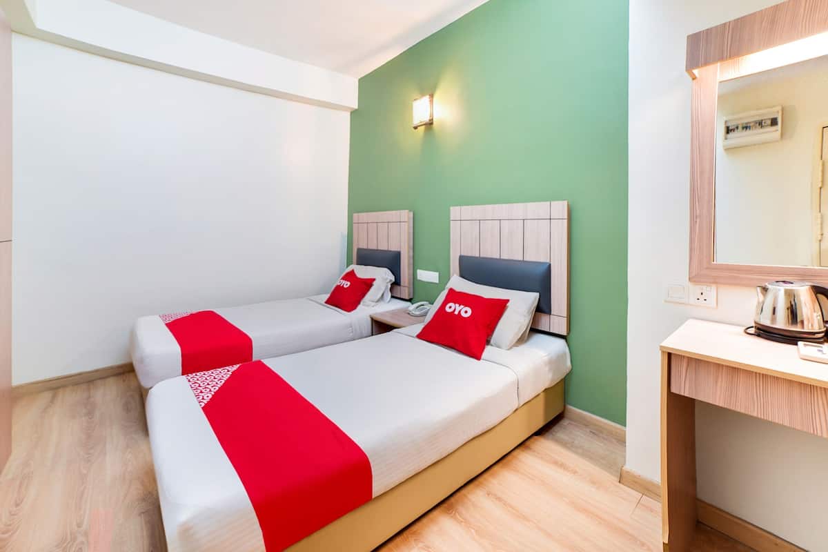 A hotel room with two beds, each with a red and white bedspread and matching pillows. There is a wooden desk with a kettle and a mirror above it.