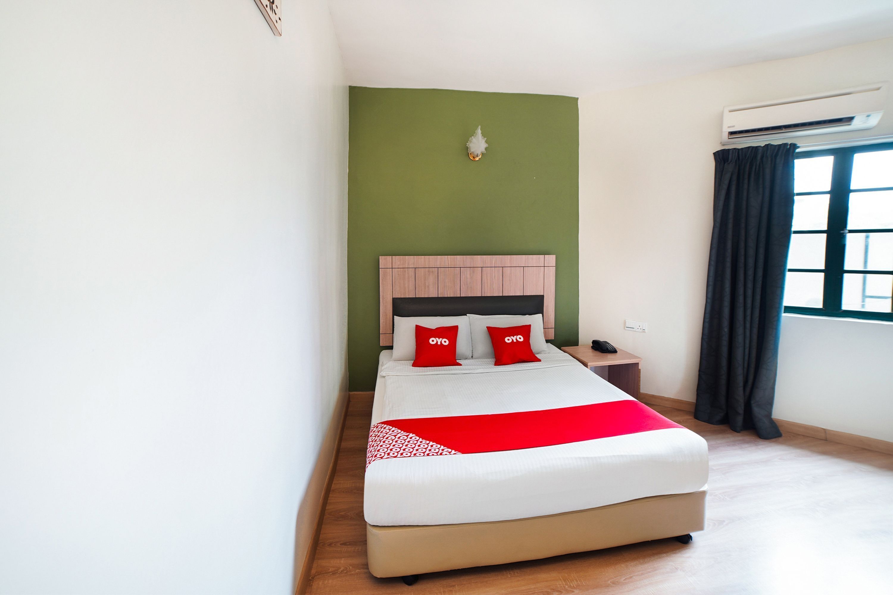 A neatly made bed with a red and white bedspread, a wooden headboard, and two red pillows with "OYO" branding.