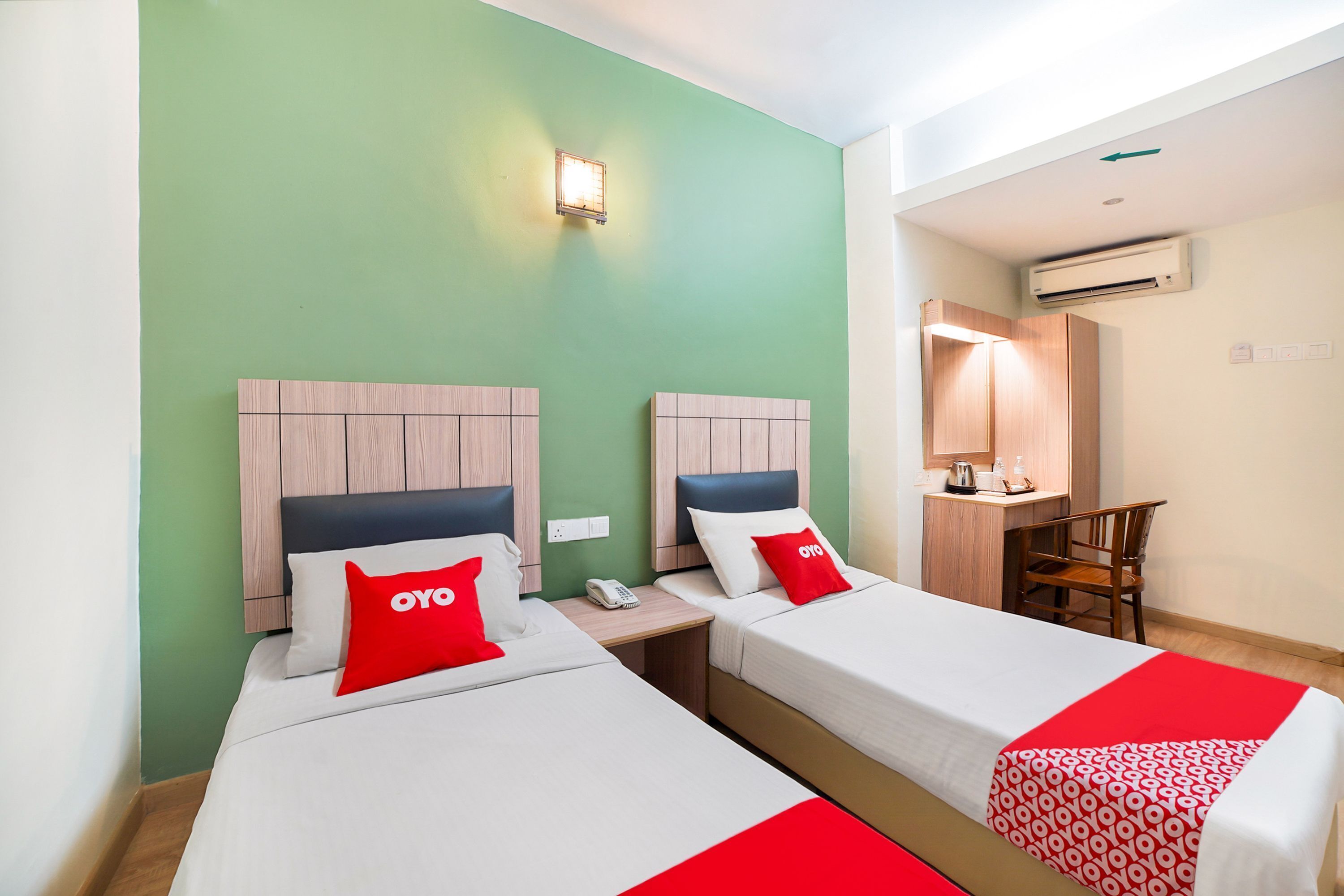 A hotel room with two beds, a desk, a chair, and a small kitchenette.