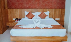A neatly made bed with a heart-shaped towel arrangement, wooden headboard, and matching nightstands with a small table and items on them.