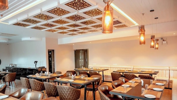 A dining area with tables and chairs, a kitchen in the background, and a decorative ceiling.