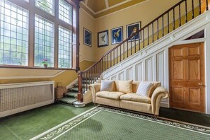 Ein Zimmer mit einem grün gemusterten Teppich, einem beigen Sofa mit Kissen, einer Holztür und einer Treppe mit Geländer.