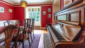Een eetkamer met een piano, rode muren en een raam met uitzicht op bomen.