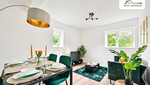 Un comedor moderno con una mesa preparada para cuatro personas, sillas tapizadas de verde, una mesa de centro negra y un amplio ventanal con vistas a la vegetación.