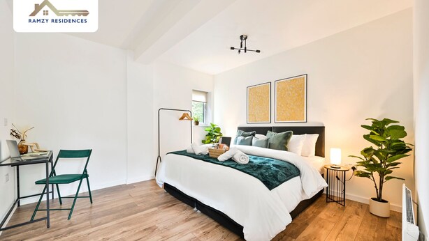 Un dormitorio con cama, escritorio, silla, lámpara de pie y planta en maceta.