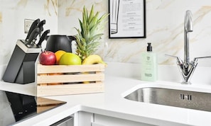 Una cocina con encimera blanca, un lavamanos con grifo moderno, una cesta de fruta y un bloque para cuchillos.