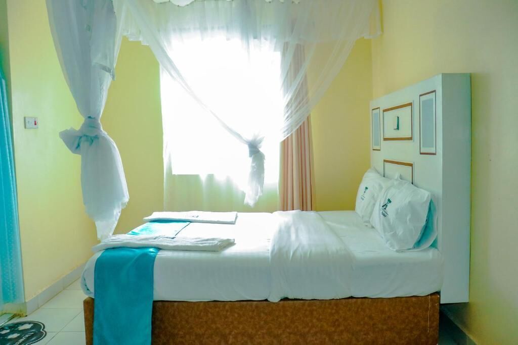 Una habitación de hotel con cama, ventana con cortinas, mesita de noche y un cuadro en la pared.