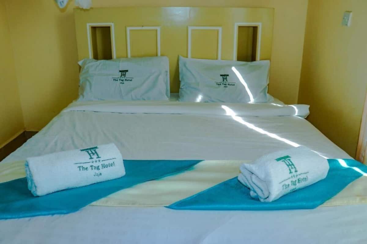 A hotel room with a bed, pillows, and towels with the hotel logo.