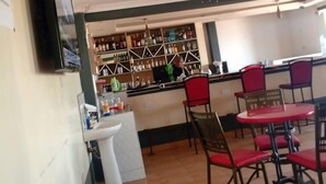 A restaurant with a bar area, red chairs, a white sink, and a ceiling fan. - The Tag Hotel  (Juja)