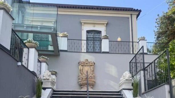 A modern building with a central staircase leading to a gated entrance, flanked by decorative stone elements and a glass facade. - Stanze letterarie  (Catania)