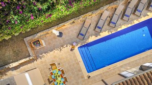 Vista aérea de una zona de piscina con solárium, sillones de descanso y una mesa de comedor.
