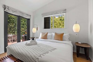 A bedroom with a bed, bedside tables, a window, and a view of the outdoors.