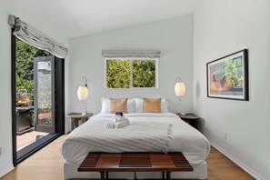 A bedroom with a bed, two bedside lamps, a window with a view, a bedside table, and a bench.