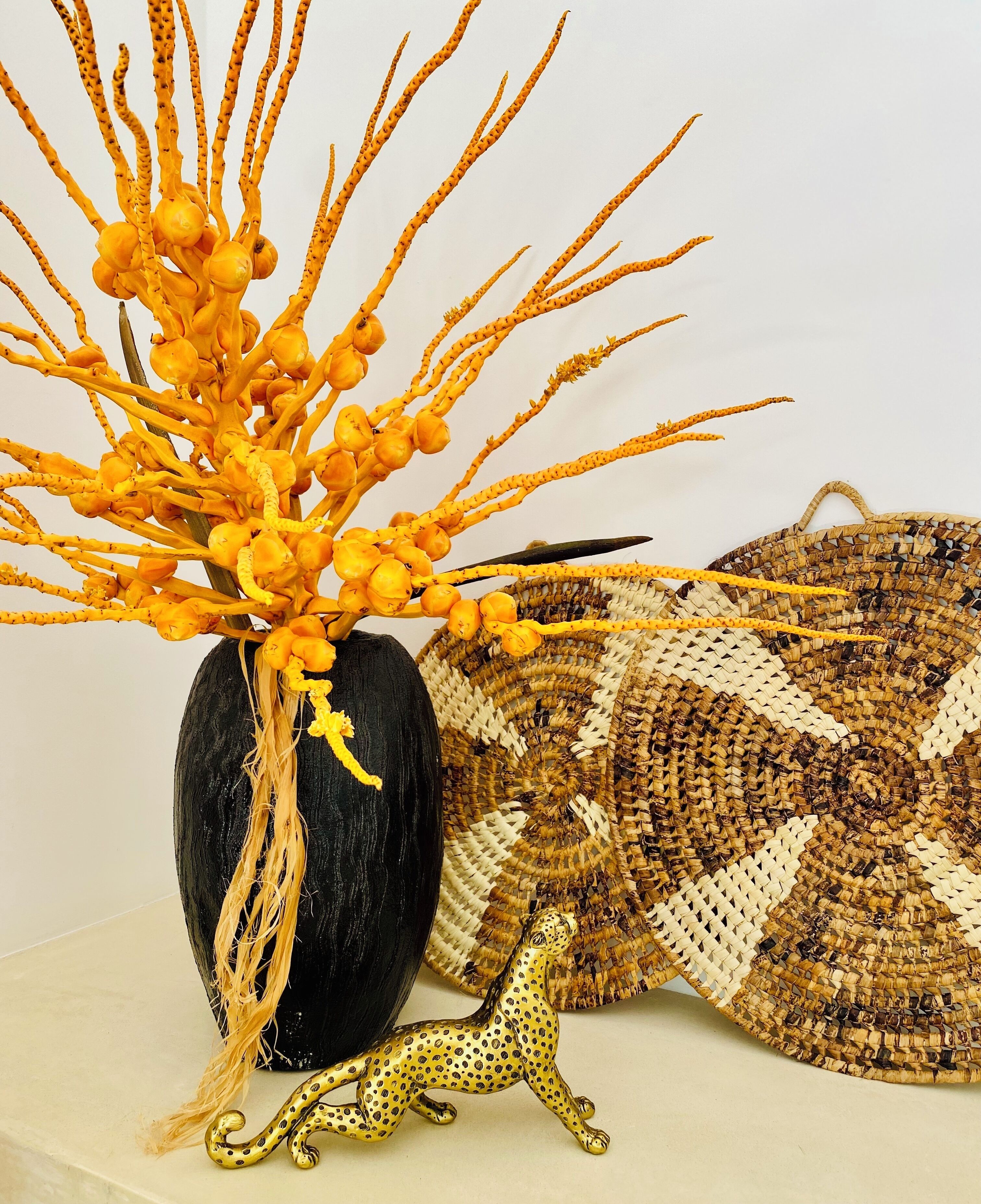 A black vase with yellow flowers, a woven basket, and a golden leopard figurine.