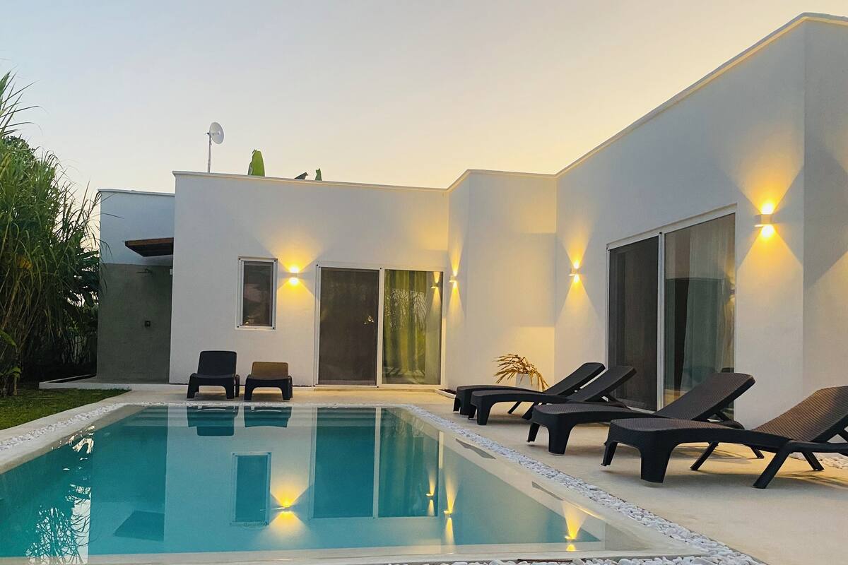 Una casa moderna con piscina, mobiliario exterior y fachada bien iluminada.