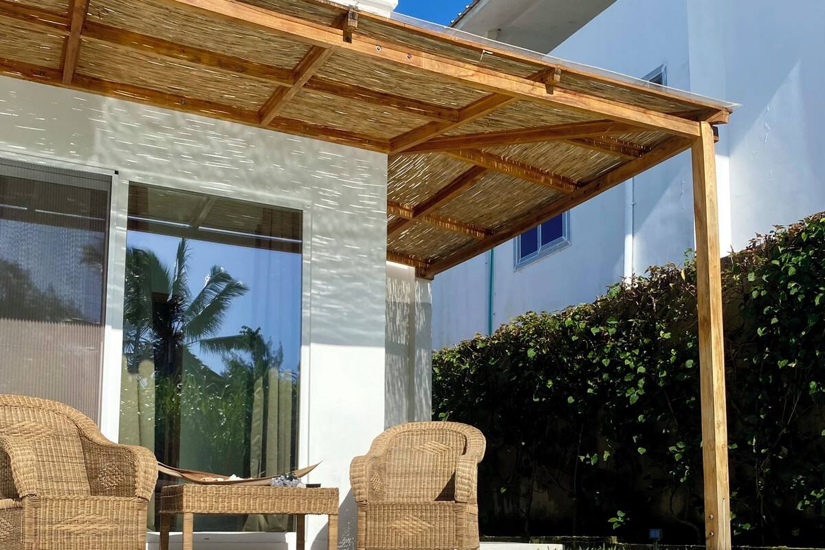 Un área de piscina exterior moderna con una pérgola, muebles de mimbre y un borde revestido de piedra.