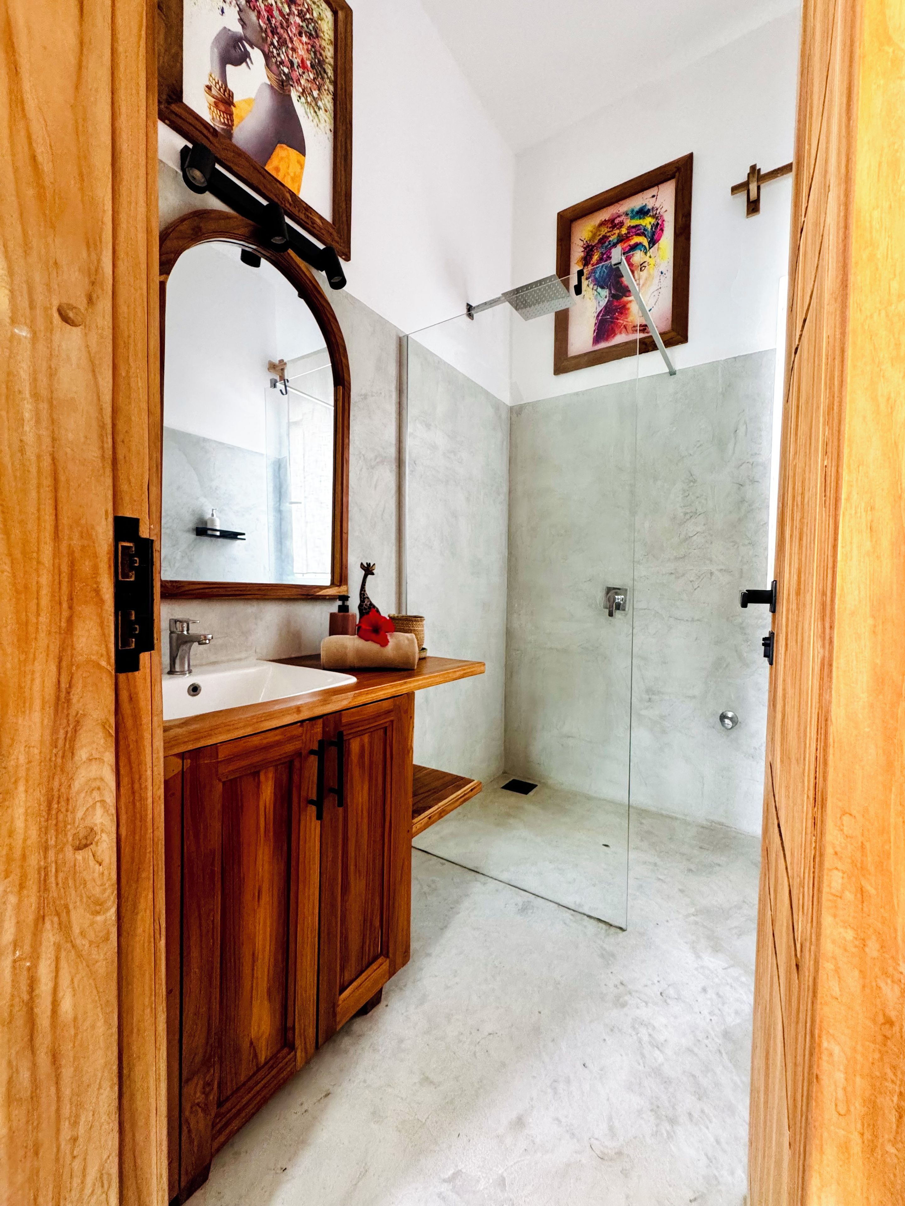 Ein Badezimmer mit einem Holzwaschtisch, einem großen Spiegel, einer Dusche mit Glastür und einem gerahmten Kunstwerk an der Wand.