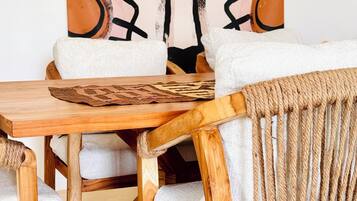 Una mesa de comedor de madera con una silla trenzada y una silla blanca acolchada. Un cuadro abstracto de gran tamaño adorna la pared detrás de la mesa.