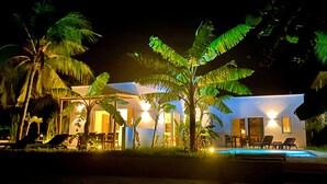 Propiedad frente a la playa de noche con piscina, palmeras y un edificio bien iluminado.