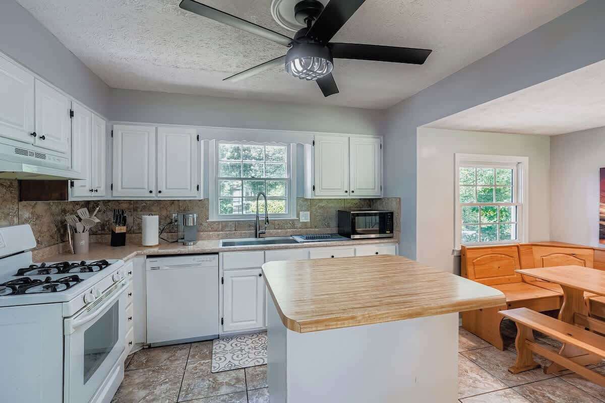 A kitchen with white cabinets, a stove, a microwave, and a wooden dining table.