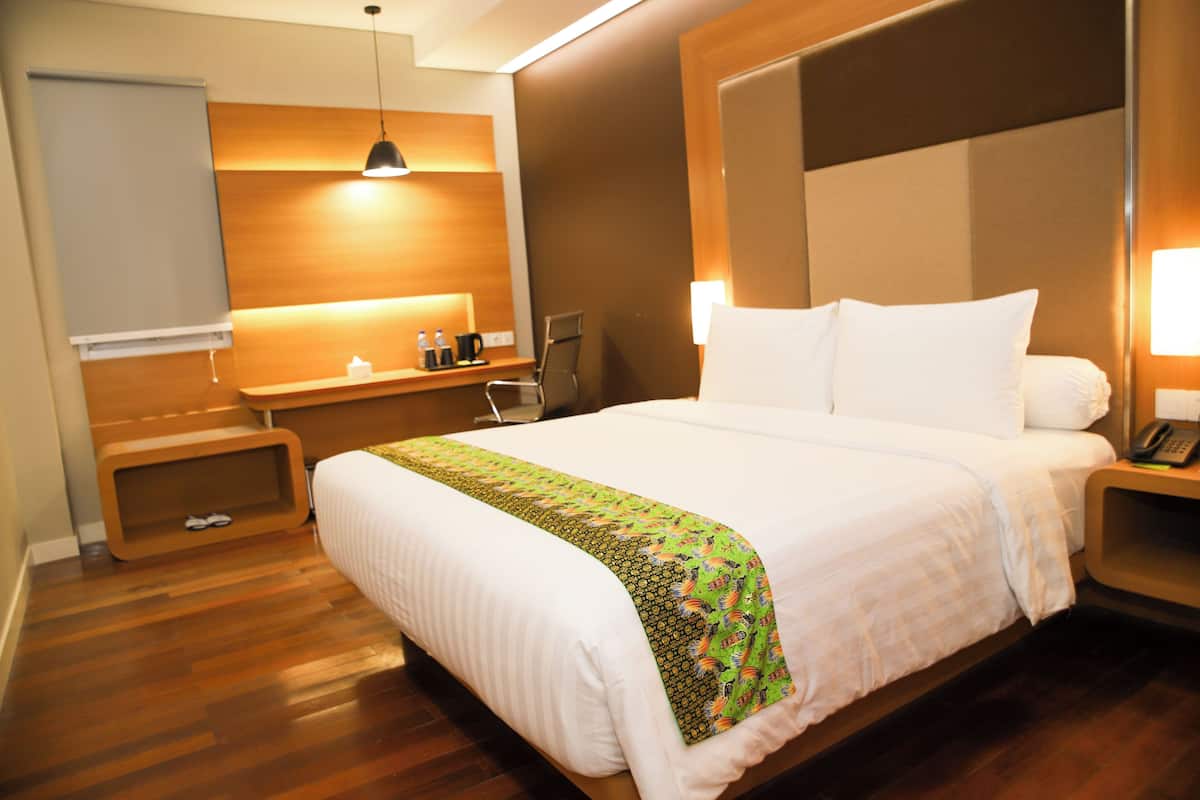 A hotel room with a large bed, bedside tables, a desk, a chair, a lamp, and a small shelf with toiletries.