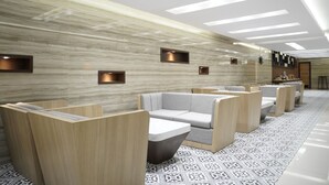 A modern waiting area with wooden partitions, cushioned seating, and patterned flooring. - Front One Hotel Papua Lestari (Timika)