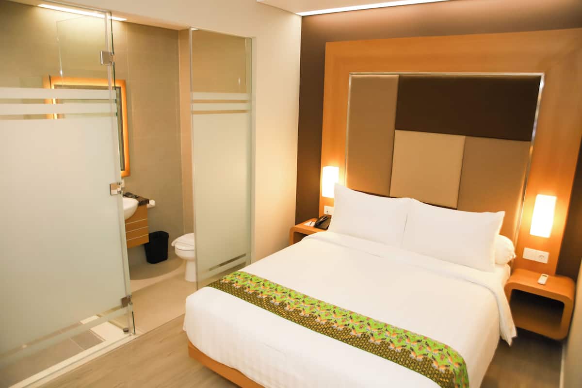 A hotel room with a bed, bedside tables, a nightstand, a mirror, a toilet, and a shower area.