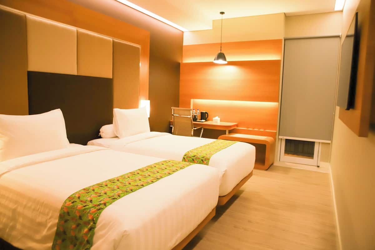 A hotel room with two beds, a desk, a chair, a small table, a lamp, and a television.