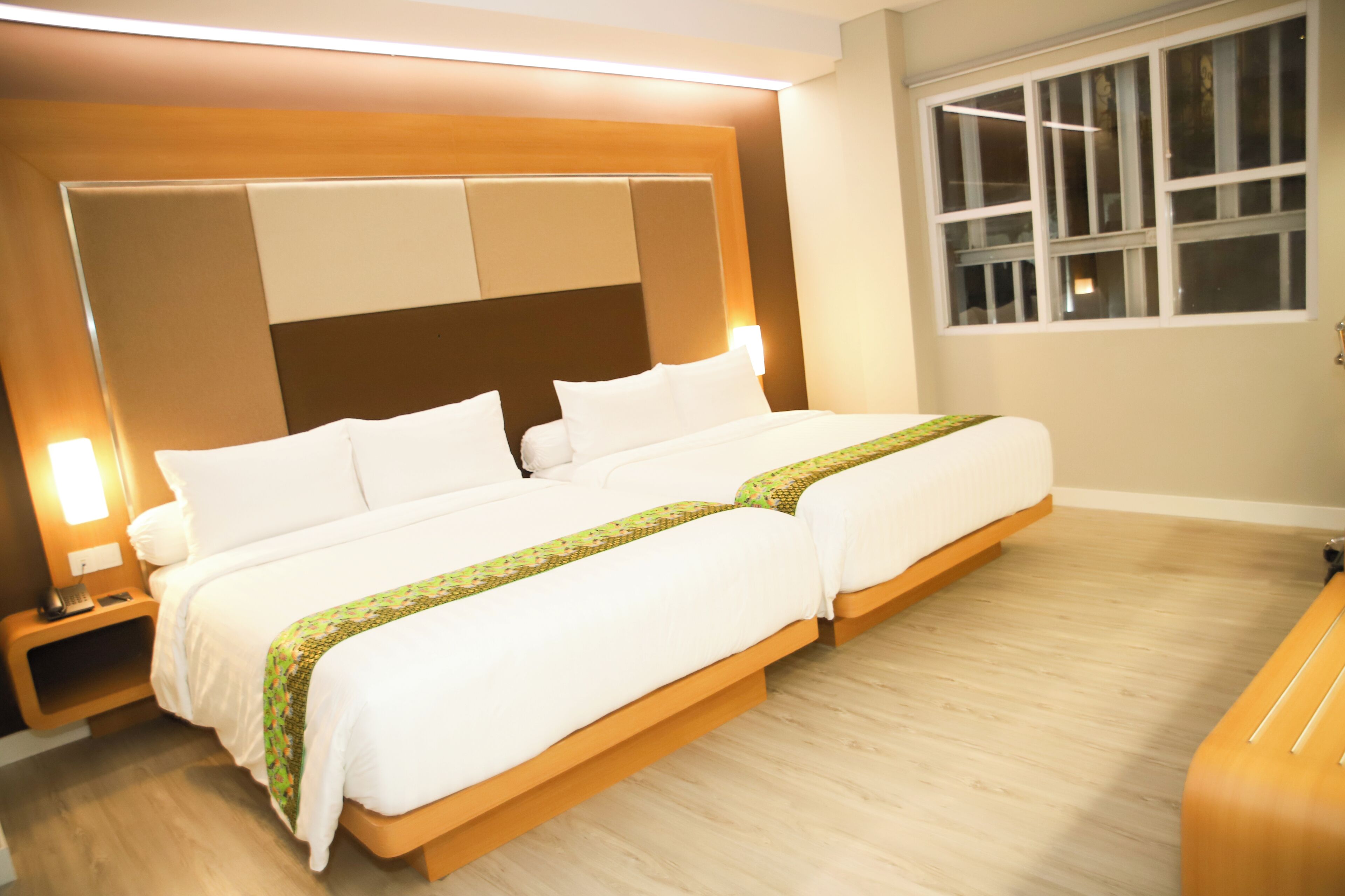 A hotel room with a large bed, a wooden headboard, a nightstand, and a window.