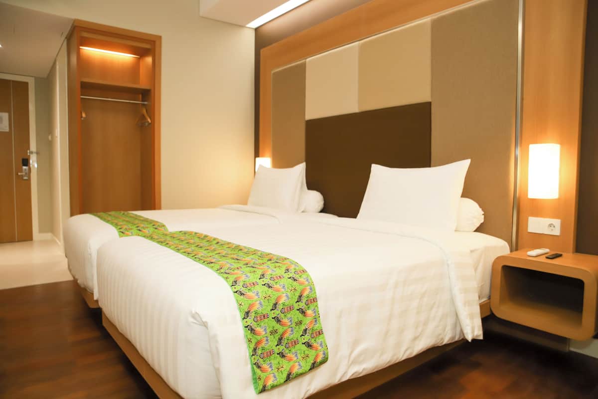 A hotel room with a large bed, a wooden headboard, a bedside table with a lamp, and a door to the left.