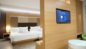 A modern hotel room with a large bed, a flat-screen TV mounted on the wall, and a wooden accent wall. - Front One Hotel Papua Lestari (Timika)