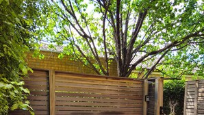 An outdoor patio with wicker furniture, including two chairs and a table, set against a wooden fence and a tiled floor. - Quiet, peaceful northcote 1 bedroom unit (Northcote)