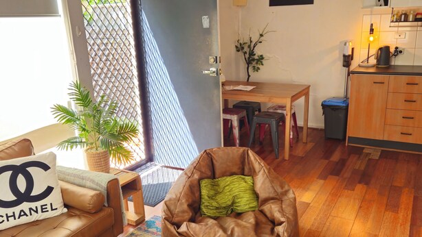 A cozy living room with a brown leather sofa, a bean bag chair, a coffee table, and a TV. There's a dining area with a table and chairs, and a kitchen area with cabinets and a countertop. - Quiet, peaceful northcote 1 bedroom unit (Northcote)
