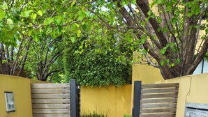A paved pathway flanked by neatly trimmed hedges and a yellow wall with a wooden gate. - Quiet, peaceful northcote 1 bedroom unit (Northcote)