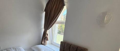 A bedroom with a bed, a nightstand, an air conditioning unit, and a window with curtains.