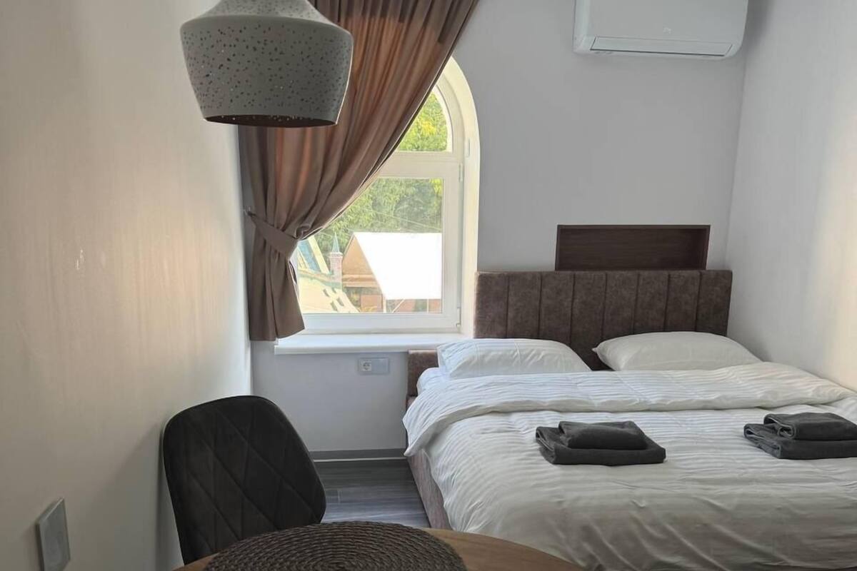 A hotel room with a bed, a desk, a chair, a remote control, and a wall-mounted air conditioner.